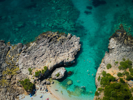 Aerial view of Aquarium Beach with turquoise water and rocky cliffs where people are swimming in a small cove in Jala Vlore County Albania. Aerial view of Aquarium Beach with turquoise water and rocky cliffs where people are swimming in a small cove in Jala Vlore County Albania.