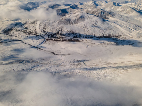 Aerial view of Babusar Pass featuring snow covered mountain peaks and a winding road under soft clouds in Babusar KPK Pakistan.