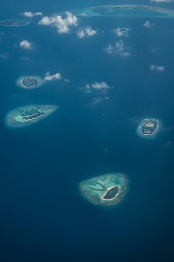 Aerial view of scattered islands amidst the vast deep blue ocean each ringed by vibrant turquoise shallows Flight from Male to Hanimaadhoo island Maldives.
