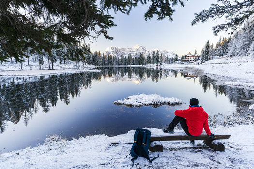 View of a lone figure in a red jacket contemplates the still reflective lake mirroring snow dusted pines and distant peaks a serene winter landscape Misurina Veneto Italy. View of a lone figure in a red jacket contemplates the still reflective lake mirroring snow dusted pines and distant peaks a serene winter landscape Misurina Veneto Italy.