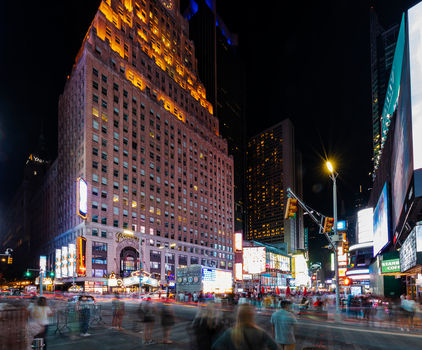 View of the illuminated Paramount Building in Times Square at night with bustling crowds and light trails from traffic in New York New York United States. View of the illuminated Paramount Building in Times Square at night with bustling crowds and light trails from traffic in New York New York United States.