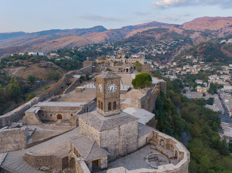 Aerial view of Gjirokaster Fortress with its iconic clock tower stone walls and historic architecture overlooking the surrounding mountains in Gjirokaster Gjirokaster County Albania. Aerial view of Gjirokaster Fortress with its iconic clock tower stone walls and historic architecture overlooking the surrounding mountains in Gjirokaster Gjirokaster County Albania.