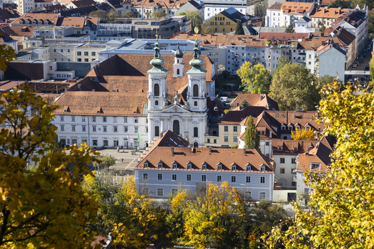View of a baroque church with twin towers and red tiled roofs nestled among buildings and autumn foliage bathed in sunlight Graz Styria Austria. View of a baroque church with twin towers and red tiled roofs nestled among buildings and autumn foliage bathed in sunlight Graz Styria Austria.