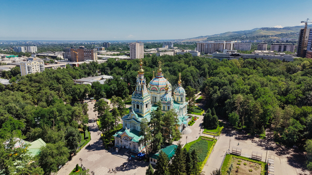 Aerial view of the colorful Ascension Cathedral surrounded by lush green trees in Panfilov Park with the urban skyline of Almaty in the background Almaty Almaty Region Kazakhstan.
