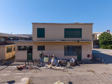 Aerial view of an old industrial building with boarded windows and scattered debris on the asphalt ground under a clear blue sky in Casale Monferrato Piedmont Italy. Aerial view of an old industrial building with boarded windows and scattered debris on the asphalt ground under a clear blue sky in Casale Monferrato Piedmont Italy.