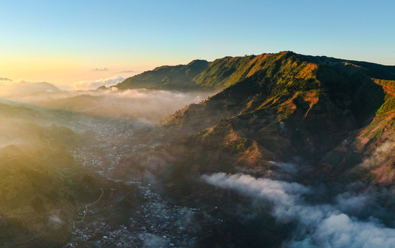 Aerial view of Dieng Plateau with terraced hills a small village nestled in the valley and morning mist illuminated by golden hour light in Indonesia.