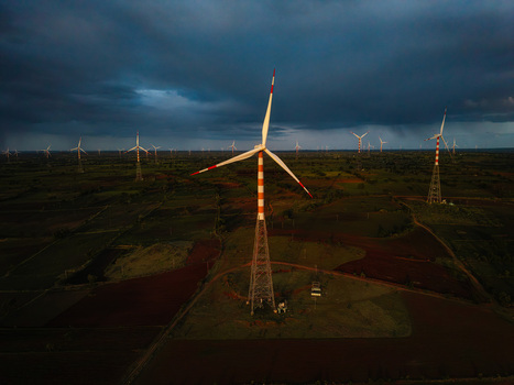 Aerial view of wind turbines standing in a vast rural landscape under a dramatic stormy sky in Hampi Karnataka India.