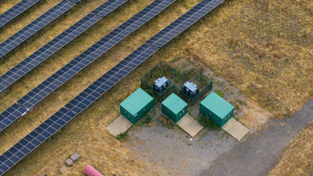 Aerial view of a solar farm featuring rows of photovoltaic panels alongside green battery storage units and electrical transformers in Bedford England United Kingdom. Aerial view of a solar farm featuring rows of photovoltaic panels alongside green battery storage units and electrical transformers in Bedford England United Kingdom.