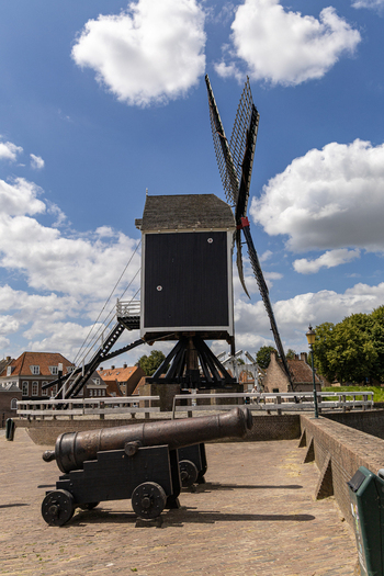 View of a historic wooden windmill and an antique iron cannon on a brick fortification wall under a blue sky with white clouds in Heusden North Brabant Netherlands.