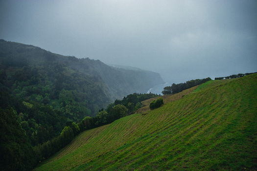 Aerial view of a rugged coastline where verdant slopes meet the moody Atlantic under a blanket of heavy sky Nordeste Azores Portugal.