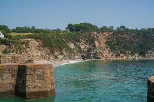 View of the historic stone harbor walls and the rugged coastline with cliffs and a small beach in Charlestown Cornwall United Kingdom. View of the historic stone harbor walls and the rugged coastline with cliffs and a small beach in Charlestown Cornwall United Kingdom.