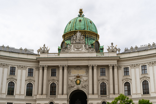View of the ornate facade and green dome of the Hofburg Palace with baroque sculptures and classical columns under an overcast sky Vienna Vienna Austria. View of the ornate facade and green dome of the Hofburg Palace with baroque sculptures and classical columns under an overcast sky Vienna Vienna Austria.