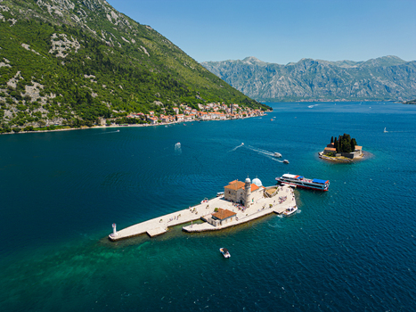 Aerial view of Our Lady of the Rocks church on a small island in the Bay of Kotor with boats and mountains in the background in Perast Kotor Municipality Montenegro. Aerial view of Our Lady of the Rocks church on a small island in the Bay of Kotor with boats and mountains in the background in Perast Kotor Municipality Montenegro.