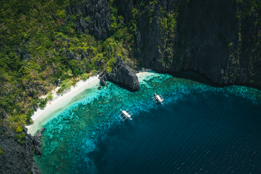 Aerial view of El Nido featuring turquoise waters limestone cliffs and traditional outrigger boats anchored near a white sand beach in El Nido Mimaropa Philippines. Aerial view of El Nido featuring turquoise waters limestone cliffs and traditional outrigger boats anchored near a white sand beach in El Nido Mimaropa Philippines.