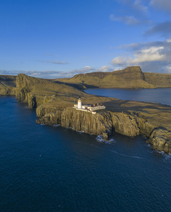 Aerial view of Neist Point Lighthouse on the edge of steep cliffs overlooking the blue sea under a clear sky Isle of Skye Scotland United Kingdom. Aerial view of Neist Point Lighthouse on the edge of steep cliffs overlooking the blue sea under a clear sky Isle of Skye Scotland United Kingdom.