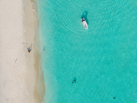 Aerial view of a pristine beach with turquoise waters meeting the shore where a boat floats gently Dhidhdhoo Thiladhunmathi Atoll Maldives.