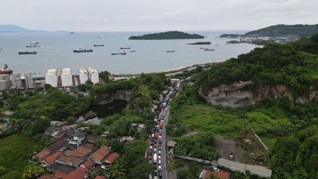 Aerial view of Merak port area featuring a road with heavy traffic industrial storage tanks a small lake and lush green hills along the coast in Pulomerak Banten Indonesia. Aerial view of Merak port area featuring a road with heavy traffic industrial storage tanks a small lake and lush green hills along the coast in Pulomerak Banten Indonesia.