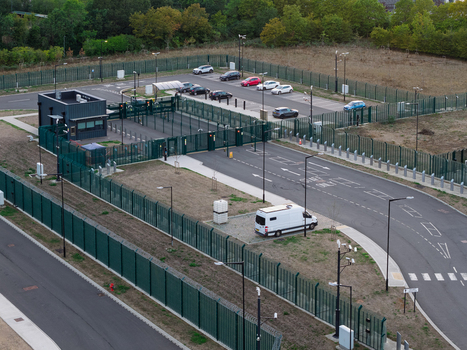 Aerial view of a secure data center entrance with a guard booth fenced perimeter parking area with cars and a white van parked near the gate in the United Kingdom. Aerial view of a secure data center entrance with a guard booth fenced perimeter parking area with cars and a white van parked near the gate in the United Kingdom.