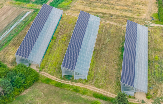 Aerial view of agricultural greenhouses with rooftop photovoltaic solar panels in rural fields illustrating agrivoltaics and clean energy in Loriol sur Drome Auvergne Rhone Alpes France.