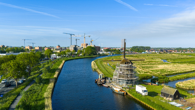 Aerial view of the Oosterdel nature reserve featuring a historic windmill under renovation beside a winding canal and lush green polder fields Broek op Langedijk Noord Holland Netherlands. Aerial view of the Oosterdel nature reserve featuring a historic windmill under renovation beside a winding canal and lush green polder fields Broek op Langedijk Noord Holland Netherlands.