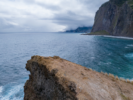 Aerial view of rocky cliffs overlooking the deep blue Atlantic Ocean under a cloudy sky in Madeira. Aerial view of rocky cliffs overlooking the deep blue Atlantic Ocean under a cloudy sky in Madeira.