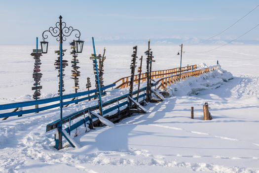 View of Goryachiye Istochniki Khakusy with wooden signposts and blue railing on a snowy pier overlooking frozen Lake Baikal in Severobaykal skiy Rayon Respublika Buryatiya Russia. View of Goryachiye Istochniki Khakusy with wooden signposts and blue railing on a snowy pier overlooking frozen Lake Baikal in Severobaykal skiy Rayon Respublika Buryatiya Russia.