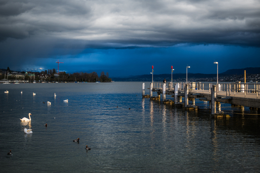 Zurich Switzerland 02 April 2023 View of a pier extending into the serene lake birds gliding on the water under a dramatic cloud laden sky. Zurich Switzerland 02 April 2023 View of a pier extending into the serene lake birds gliding on the water under a dramatic cloud laden sky.