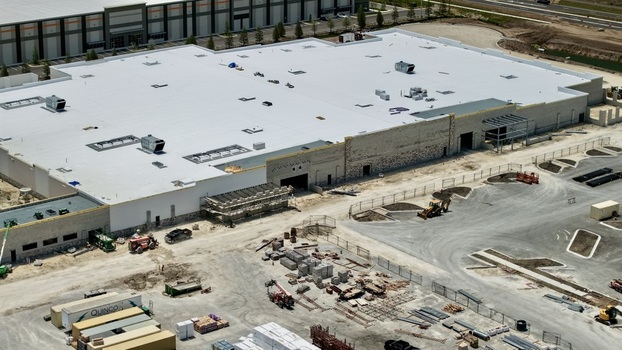 Aerial view of the large industrial warehouse construction site at Foundry Lane featuring a white flat roof and heavy machinery World Golf Village Florida United States.
