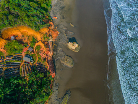 Aerial view of the rugged coastline featuring vibrant orange cliffs dark sandy beach and crashing waves along the shore in Bali Indonesia. Aerial view of the rugged coastline featuring vibrant orange cliffs dark sandy beach and crashing waves along the shore in Bali Indonesia.