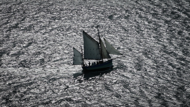 Aerial view of a sailboat gliding on the sea with sparkling sunlight reflecting on the water s surface Carantec Finistere France. Aerial view of a sailboat gliding on the sea with sparkling sunlight reflecting on the water s surface Carantec Finistere France.