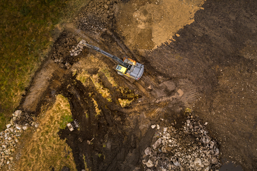 Aerial view of an excavator working in a muddy field with piles of rocks and excavated soil Jaeren Norway.
