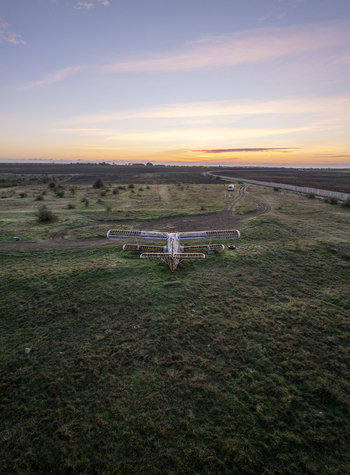 Aerial view of an abandoned skeletal biplane resting in a grassy field during a vibrant sunset in Bulgaria. Aerial view of an abandoned skeletal biplane resting in a grassy field during a vibrant sunset in Bulgaria.
