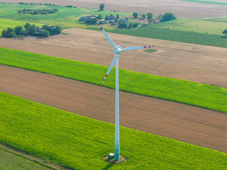 Aerial view of a wind turbine standing in the middle of vibrant green and brown agricultural fields in the rural landscape of Poland.