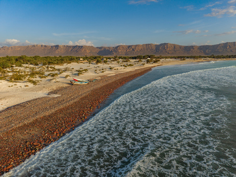 Aerial view of the rugged coastline where the sandy beach meets the turquoise sea contrasting with the barren mountains in the distance Kadrihnitin Socotra Yemen. Aerial view of the rugged coastline where the sandy beach meets the turquoise sea contrasting with the barren mountains in the distance Kadrihnitin Socotra Yemen.