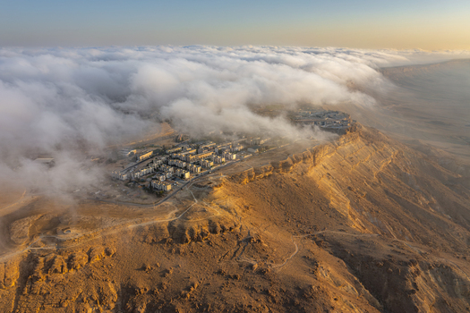 Aerial view of Mitzpe Ramon crater partially covered by low hanging clouds at golden hour showcasing the desert landscape and town in Mitzpe Ramon South District Israel. Aerial view of Mitzpe Ramon crater partially covered by low hanging clouds at golden hour showcasing the desert landscape and town in Mitzpe Ramon South District Israel.