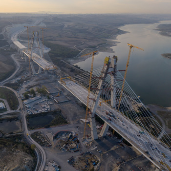 Aerial view of a large cable stayed bridge under construction with tall cranes concrete pylons and steel cables extending over a reservoir in Istanbul Istanbul Turkiye.