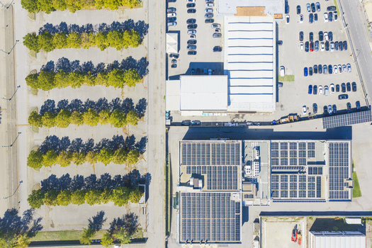 Aerial view of a parking lot with rows of trees alongside a commercial building featuring extensive solar panel installations on the roof in Arezzo Tuscany Italy. Aerial view of a parking lot with rows of trees alongside a commercial building featuring extensive solar panel installations on the roof in Arezzo Tuscany Italy.