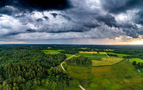 Aerial view of lush green forests and agricultural fields in Latvia under a dramatic dark storm sky with heavy clouds and rain showers in the distance Latvia. Aerial view of lush green forests and agricultural fields in Latvia under a dramatic dark storm sky with heavy clouds and rain showers in the distance Latvia.