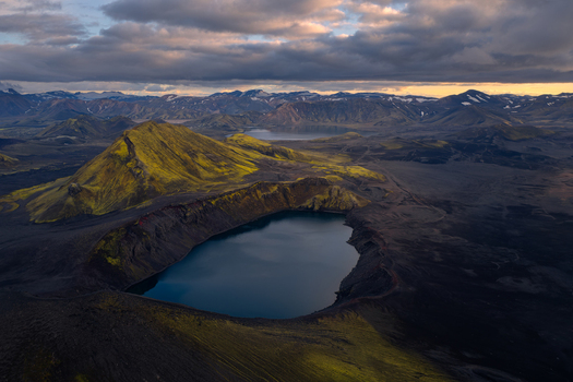 Aerial view of the volcanic crater lake in the Iceland Highlands surrounded by moss covered hills and rugged mountains under a dramatic cloudy sky. Iceland Iceland. Aerial view of the volcanic crater lake in the Iceland Highlands surrounded by moss covered hills and rugged mountains under a dramatic cloudy sky. Iceland Iceland.