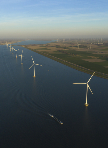 Aerial view of wind turbines in a row in the water next to a canal with a cargo barge and green fields at sunset Netherlands. Aerial view of wind turbines in a row in the water next to a canal with a cargo barge and green fields at sunset Netherlands.