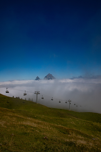 View of the Swiss Alps rising above a sea of clouds with a cable car line crossing the grassy slopes of Airolo Ticino Switzerland. View of the Swiss Alps rising above a sea of clouds with a cable car line crossing the grassy slopes of Airolo Ticino Switzerland.