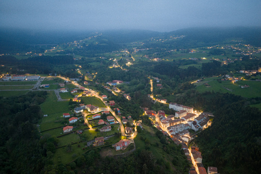Aerial view of the illuminated town of Cudillero nestled among lush green hills under a misty twilight sky in Cudillero Asturias Spain. Aerial view of the illuminated town of Cudillero nestled among lush green hills under a misty twilight sky in Cudillero Asturias Spain.