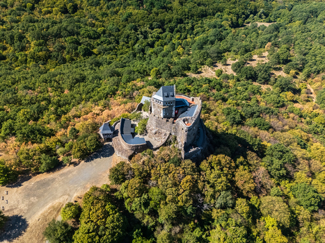 Aerial view of Holloko Castle a medieval stone fortress with defensive walls and towers surrounded by late summer forest on a wooded hill in Holloko Hungary. Aerial view of Holloko Castle a medieval stone fortress with defensive walls and towers surrounded by late summer forest on a wooded hill in Holloko Hungary.