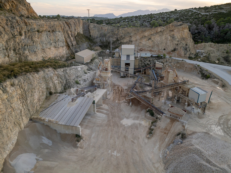 Aerial view of a stone quarry with industrial processing machinery conveyor belts and piles of gravel set against rocky cliffs in Teulada Valencian Community Spain.