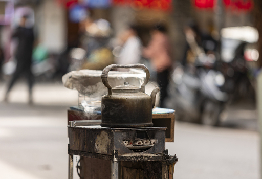 View of a steaming metal kettle resting on a small charcoal stove on a busy street in Hanoi Ha Noi Vietnam.