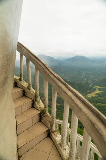 View of the narrow spiral staircase of Ambuluwawa Tower overlooking lush green hills and misty mountains under a cloudy sky in Gampola Central Province Sri Lanka. View of the narrow spiral staircase of Ambuluwawa Tower overlooking lush green hills and misty mountains under a cloudy sky in Gampola Central Province Sri Lanka.