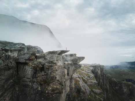 Aerial view of a person standing on the edge of the rocky Hellemojuvet canyon surrounded by mist and dramatic mountains in Hellmobotn Nordland Norway. Aerial view of a person standing on the edge of the rocky Hellemojuvet canyon surrounded by mist and dramatic mountains in Hellmobotn Nordland Norway.