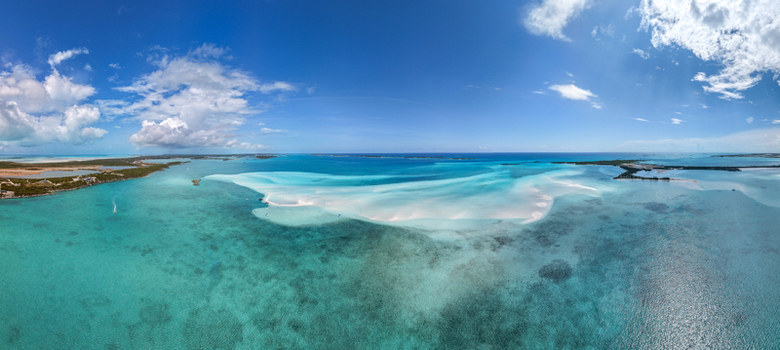 Aerial view of the Man O War Cay Sandbar surrounded by turquoise tropical waters and lush islands under a blue sky in Rolletown Exuma The Bahamas. Aerial view of the Man O War Cay Sandbar surrounded by turquoise tropical waters and lush islands under a blue sky in Rolletown Exuma The Bahamas.