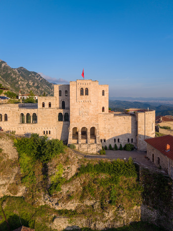 Aerial view of Kruje Castle with its historic stone walls and red flag perched on a rocky cliffside under a clear blue sky in Kruje Durres County Albania.