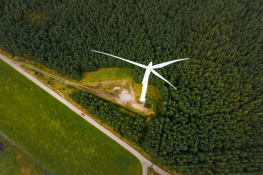 Aerial view of a white wind turbine at Hog Jaeren wind farm surrounded by a dense coniferous forest next to a road in Ha Municipality Rogaland Norway.